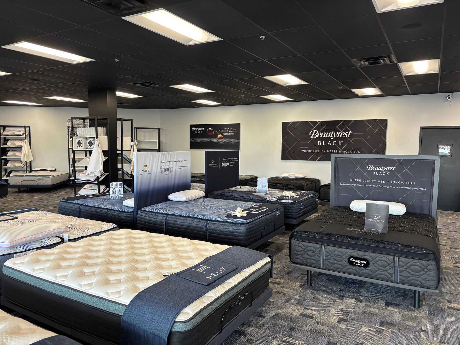 Mattress showroom with several beds displayed under bright ceiling lights