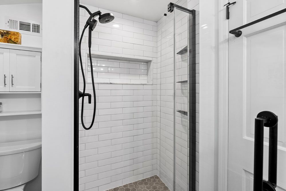White tiled shower with black hardware and glass door, next to a white door.