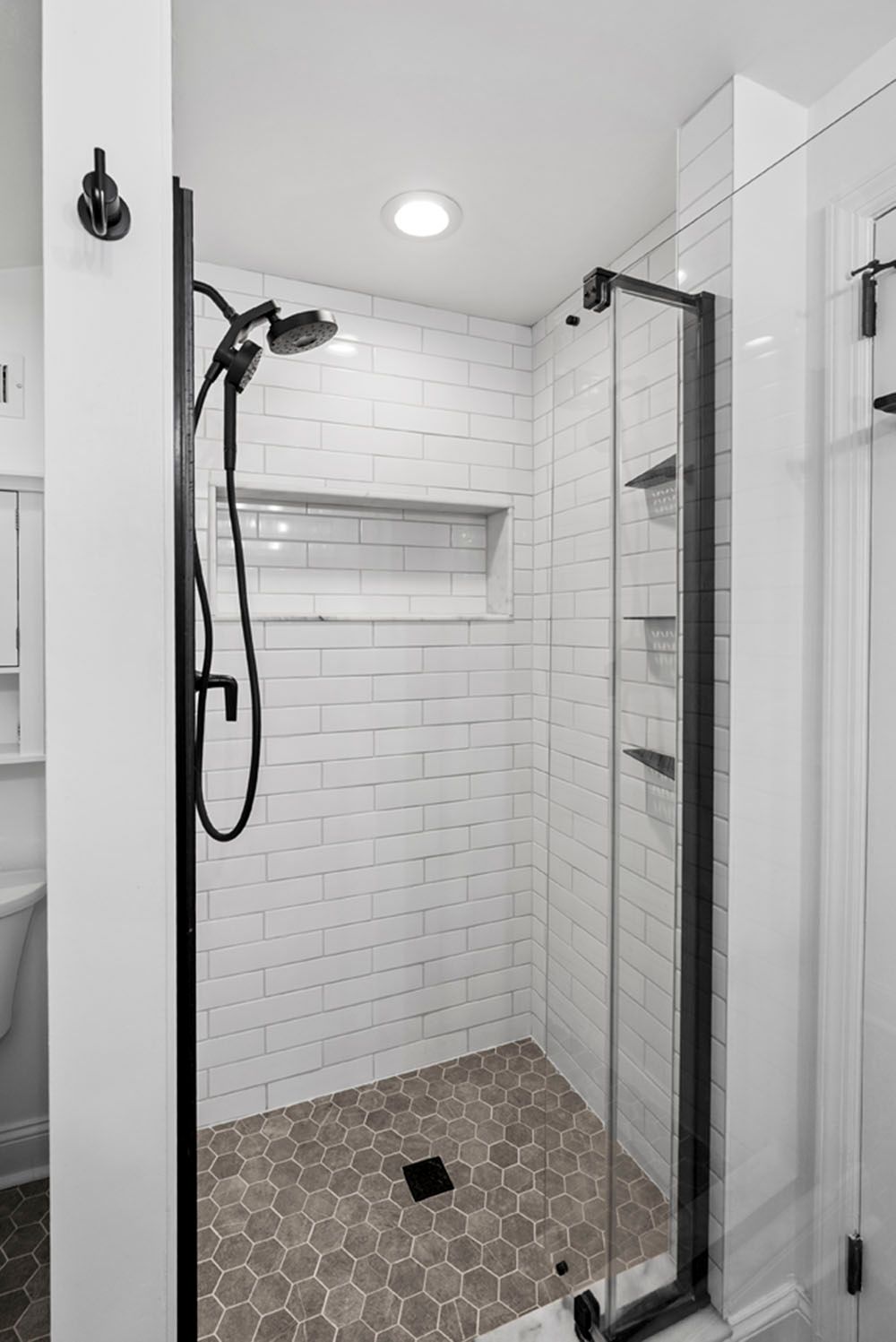 Walk-in shower with gray hexagonal tile floor, white subway tile walls, and black fixtures.