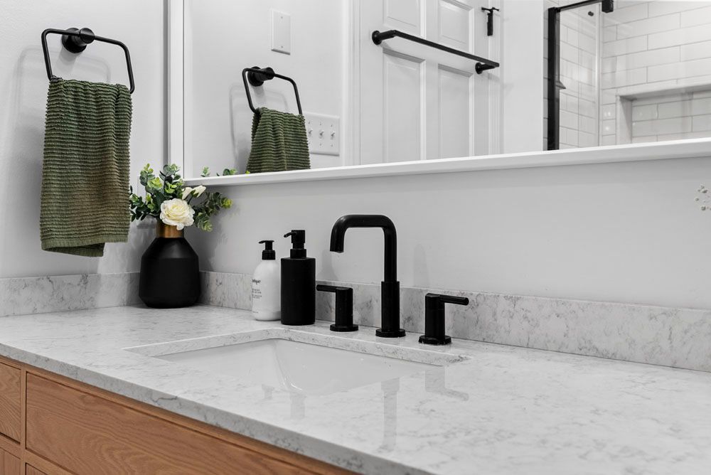 Bathroom with white countertop, black fixtures, wooden cabinet, and green towels.
