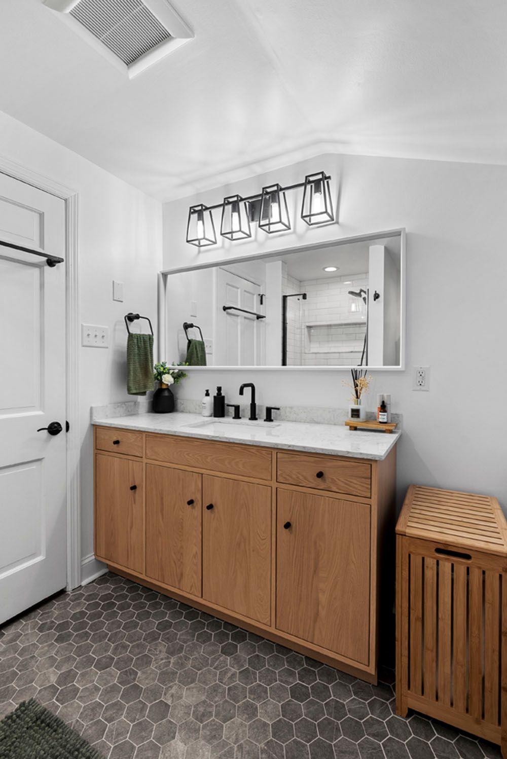 Bathroom with light wood vanity, black fixtures, and gray hexagon tile floor.