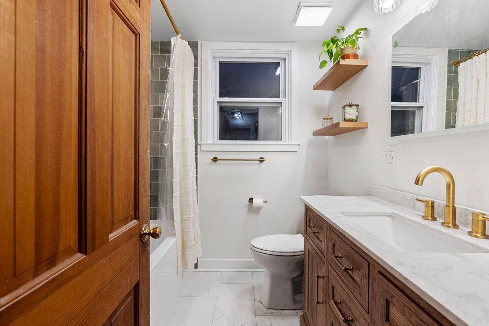 Bathroom with wooden vanity, gold fixtures, white walls, and wood door.