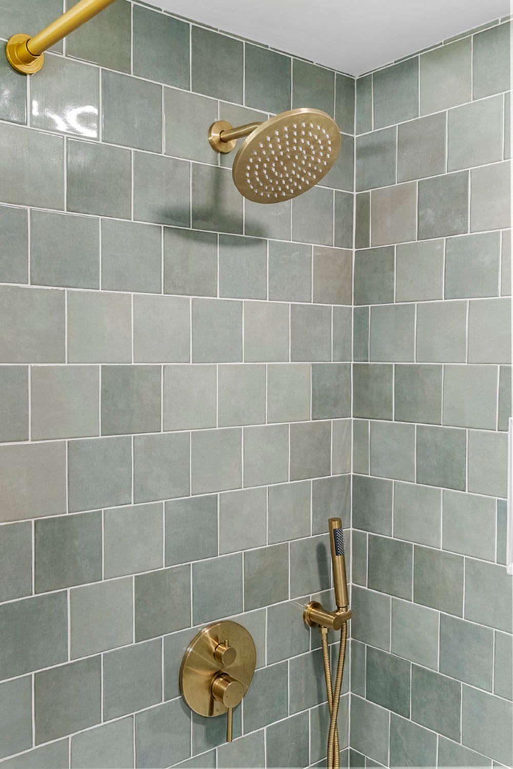 Gold shower fixtures in a shower stall with square, blue-green tiles.