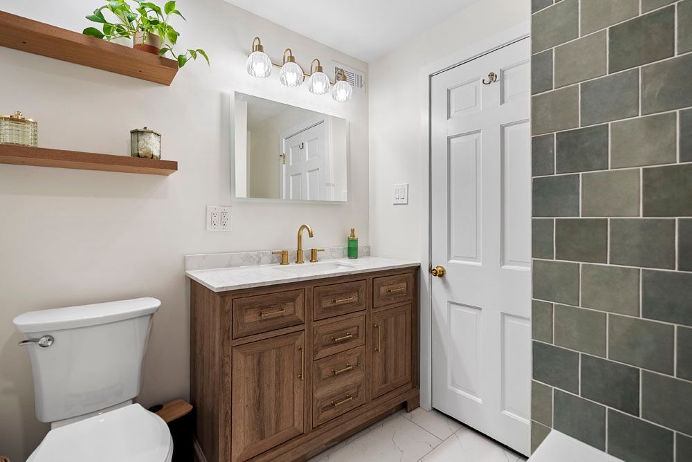 Bathroom with wooden vanity, white toilet, and green tile wall.