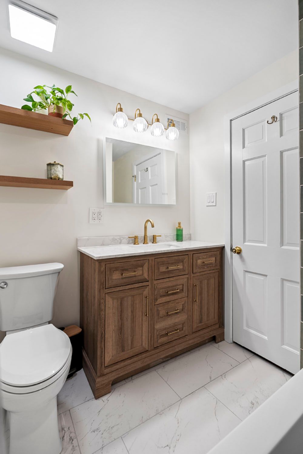 Bathroom with wooden vanity, white toilet, and floating shelves with plants.