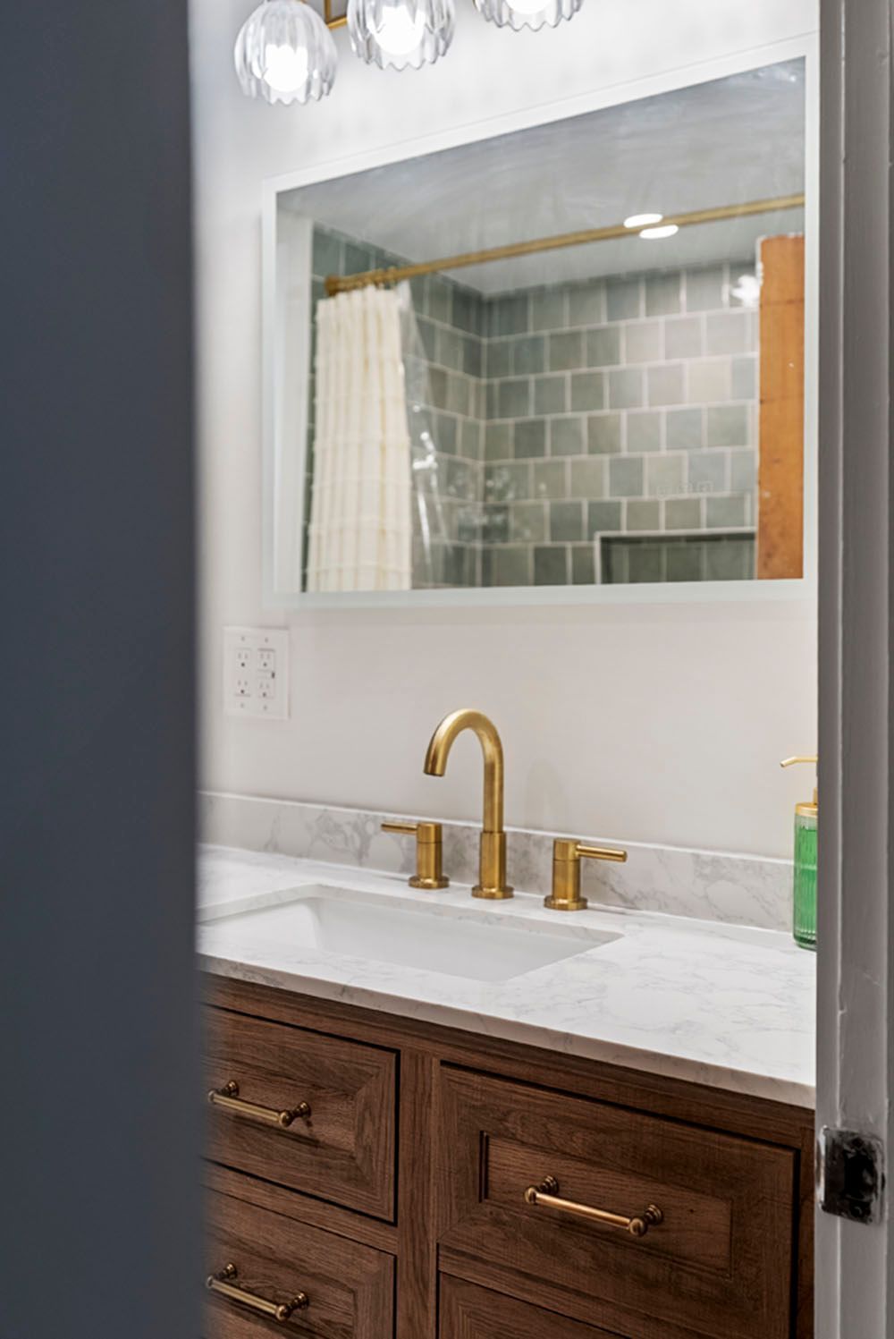 Bathroom vanity with gold faucet, mirror, brown cabinets, and white countertop.