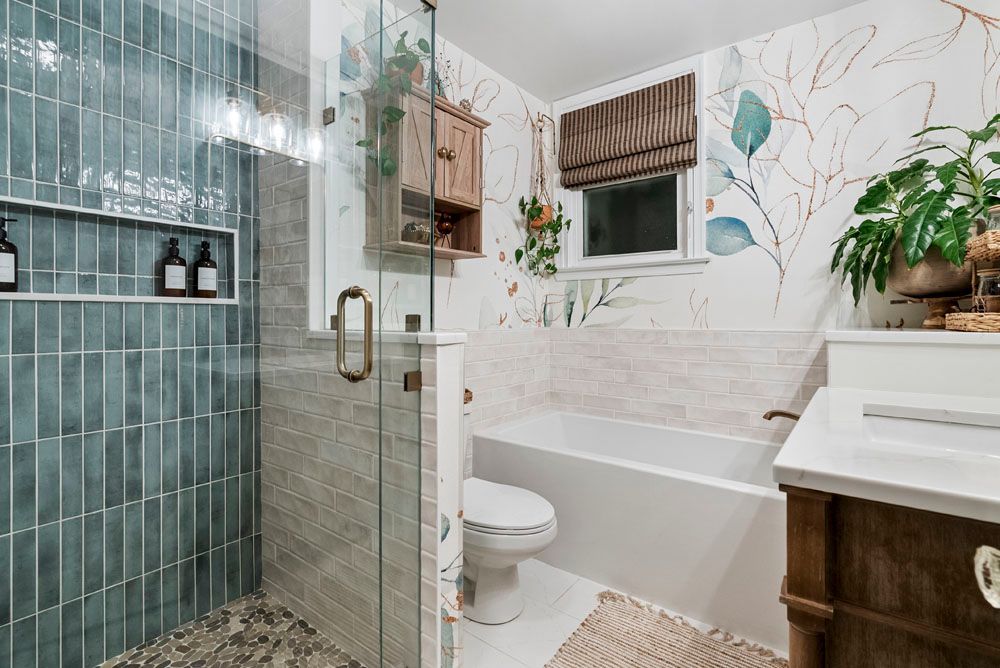 Bathroom with teal tile shower, floral wallpaper, and a white bathtub.