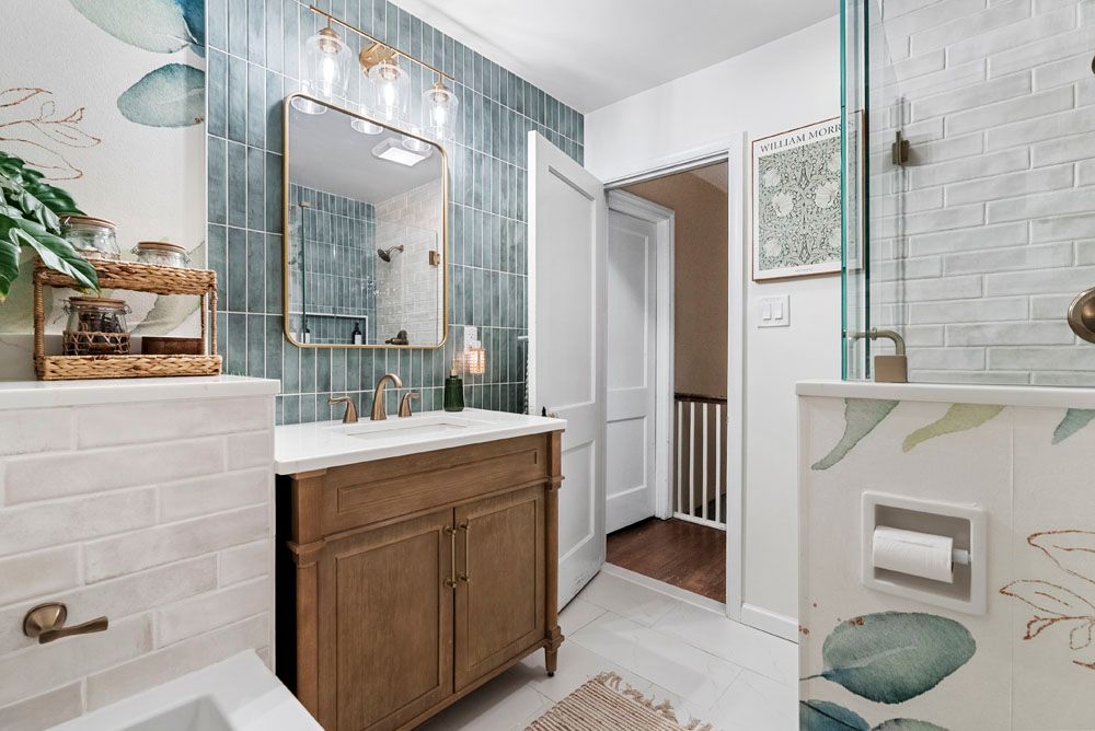 Bathroom with blue-tiled wall, wooden vanity, and glass shower door. White and teal floral wall decor.