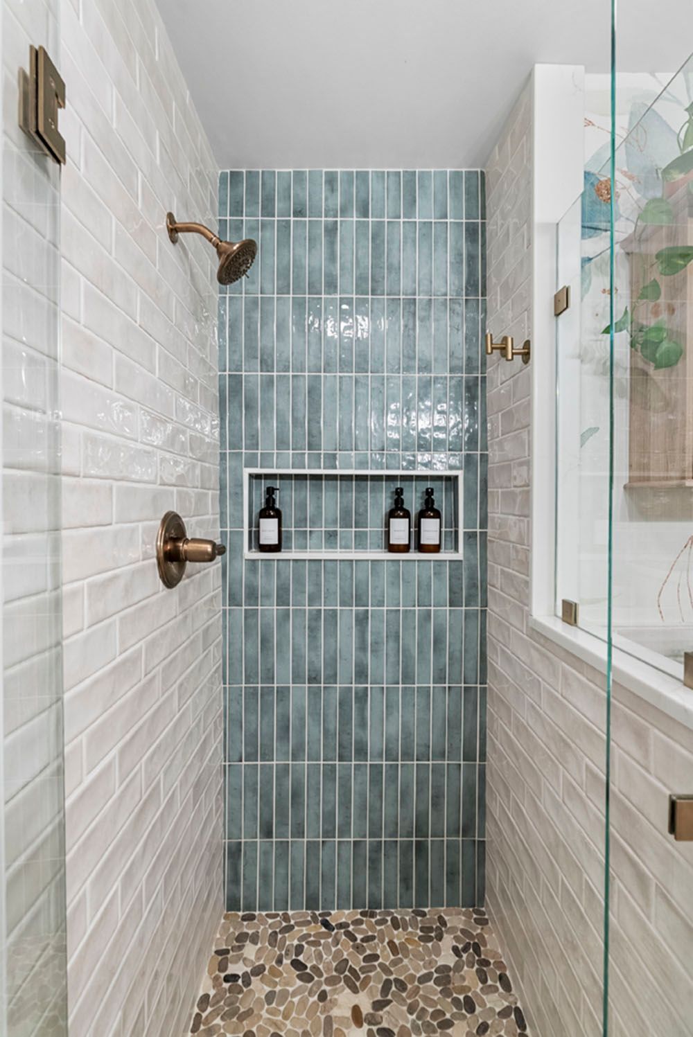 Shower with gray and teal tiles, bronze fixtures, and a pebble floor.