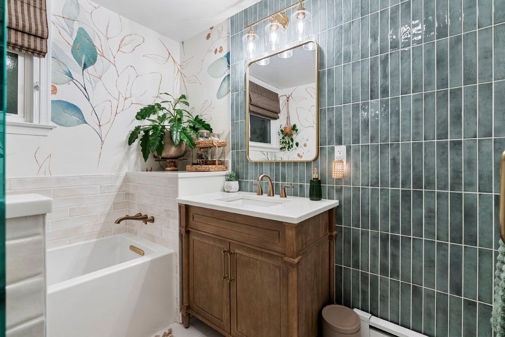 Bathroom with teal tile wall, floral wallpaper, wood vanity, and a tub.