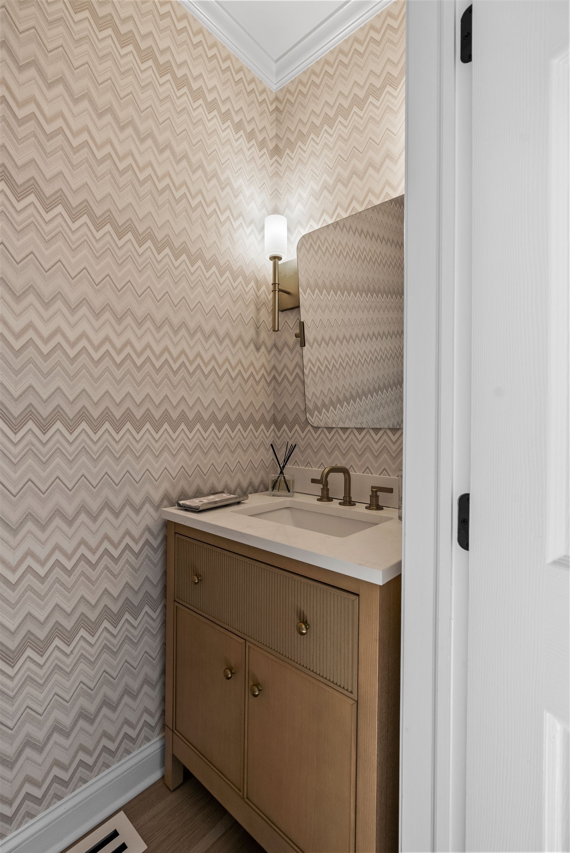 Small bathroom with zig-zag patterned wallpaper, light wood vanity, and a mirror.