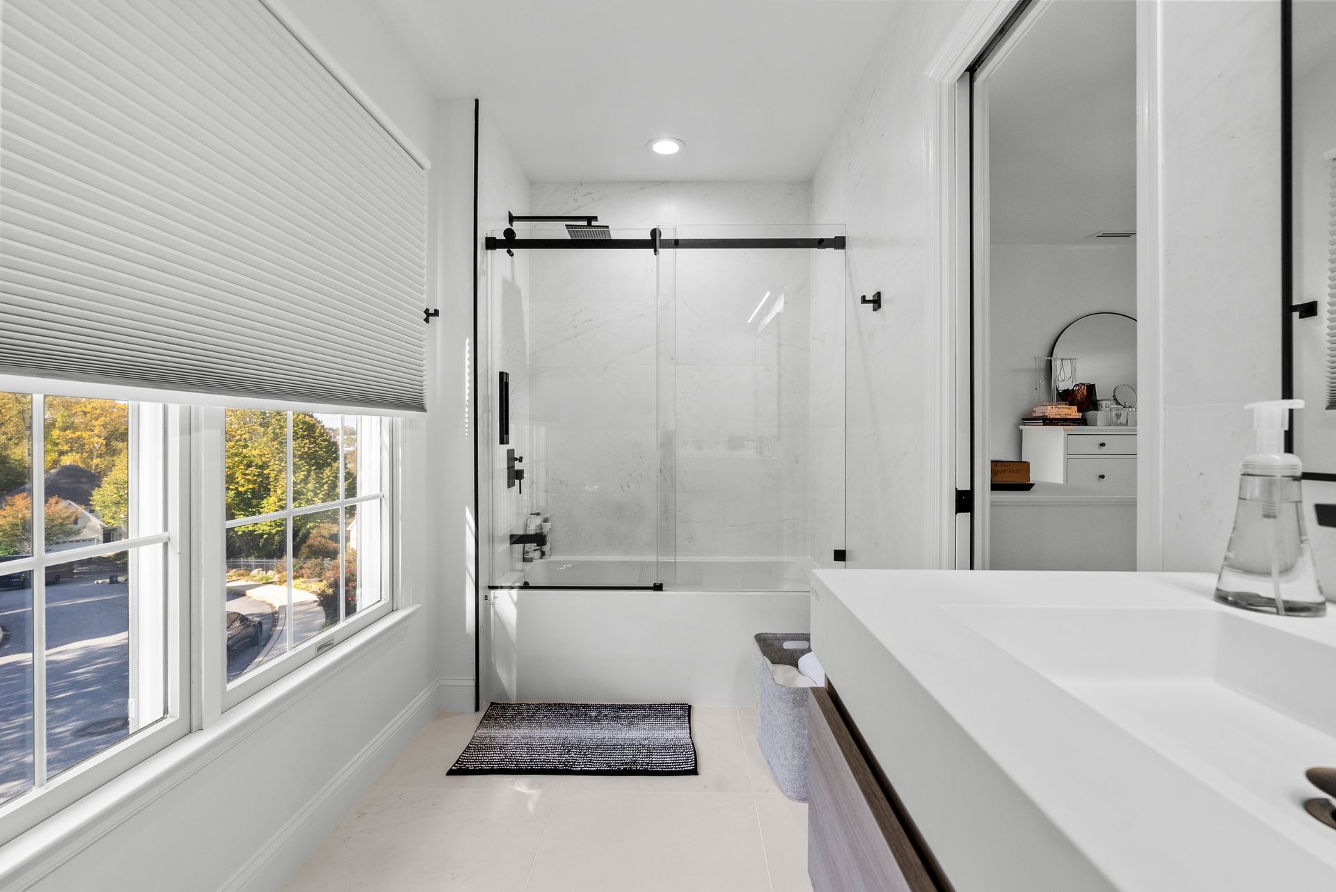 Bright white modern bathroom with a window, tub, shower, and vanity.