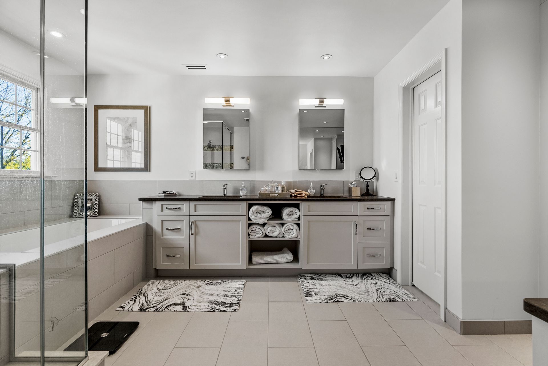 Bright white bathroom with double vanity, two mirrors, and a glass shower.