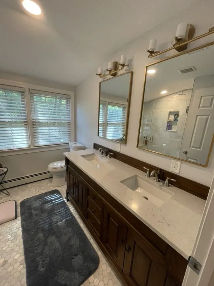 Bathroom with double sinks, two mirrors with gold frames, brown vanity, and white countertops.