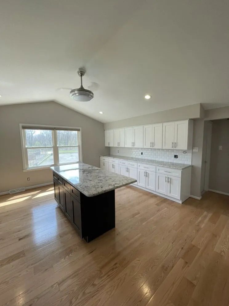 Modern kitchen with white cabinets, dark island, granite countertop, and wood floor.