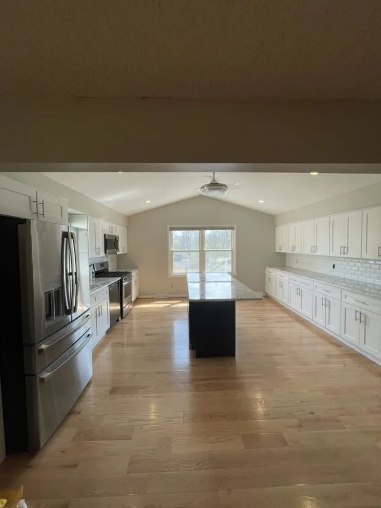 Spacious kitchen with wood floors, white cabinets, stainless steel appliances, and a black island.