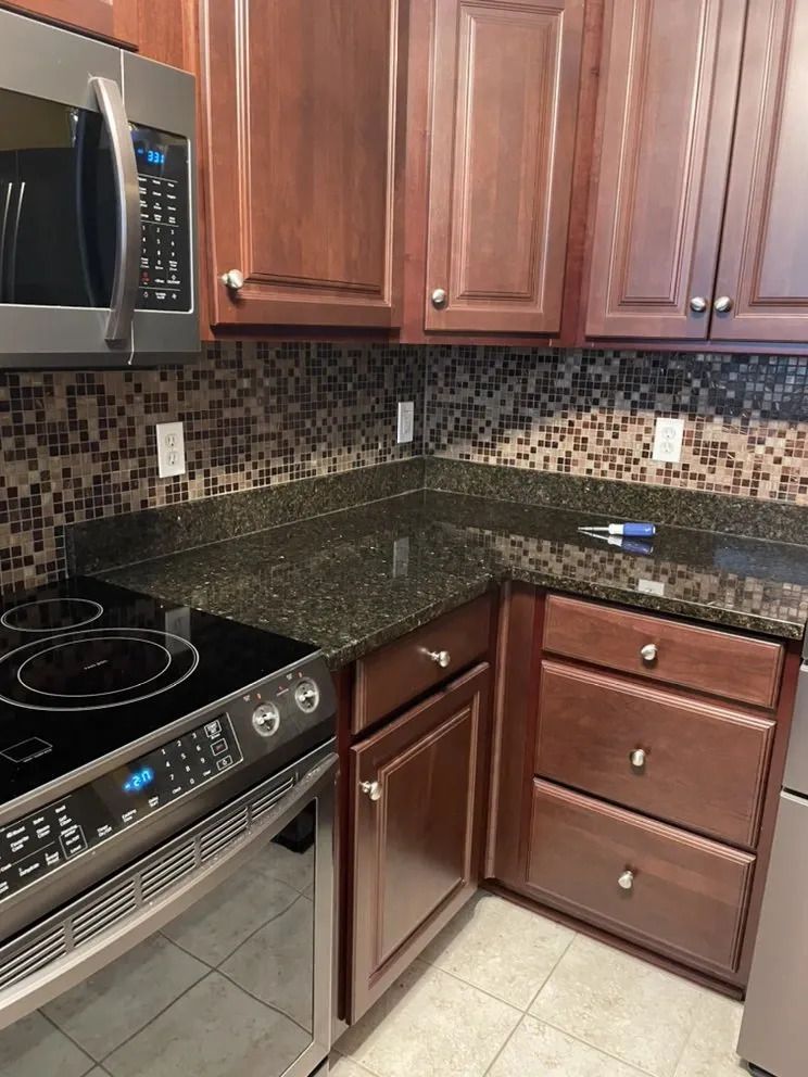 Kitchen with cherry cabinets, black granite countertops, and mosaic tile backsplash; electric stove and microwave.