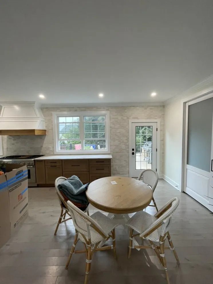 Kitchen with wooden cabinets, a round table with chairs, and a door leading outside.