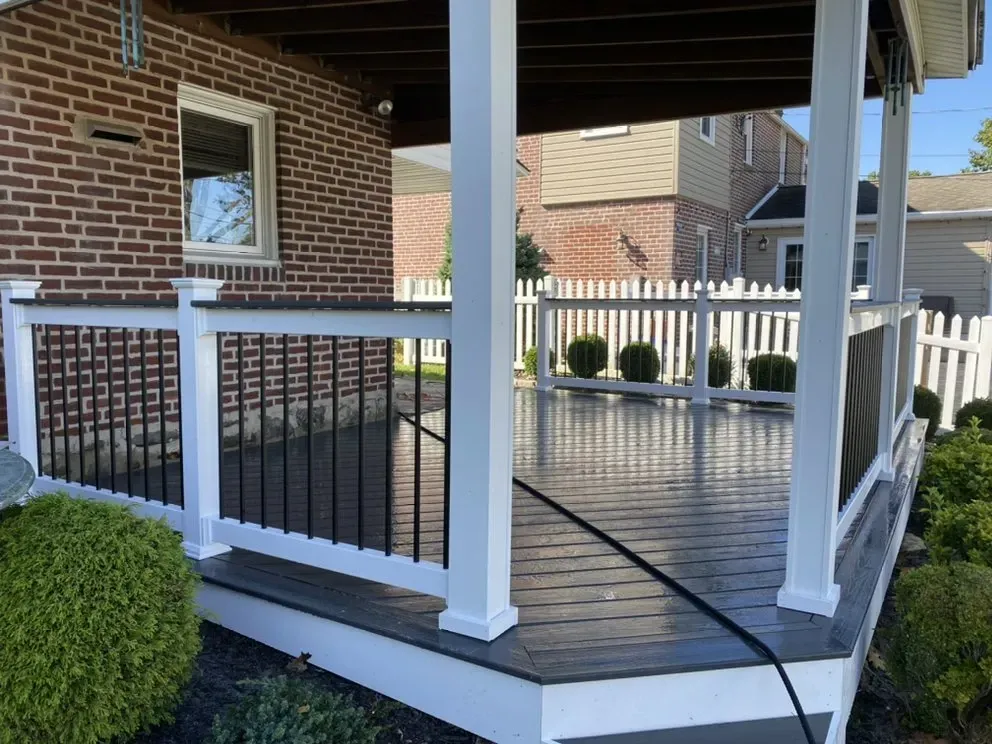 A composite deck with white railings and black balusters, beside a brick house and a white picket fence.