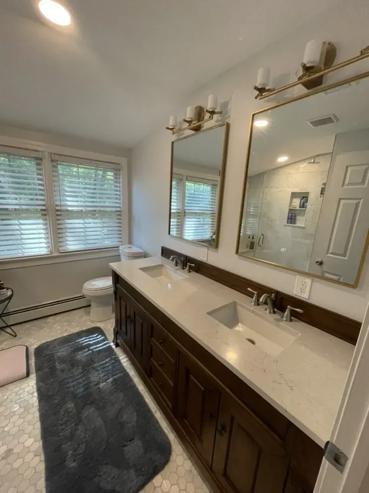 Bathroom with double vanity, mirrors, and a window. Brown cabinets, white countertops, and hexagon tile floor.