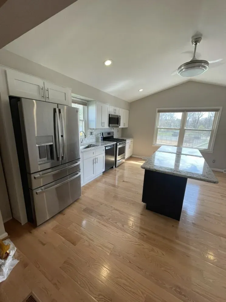 Modern kitchen with white cabinets, stainless steel appliances, light wood floors, and black island with granite counter