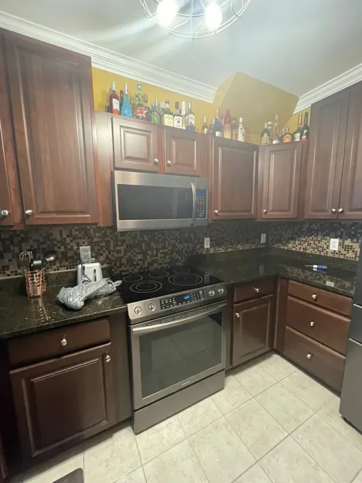 Dark wood kitchen cabinets, stainless steel appliances, dark countertops, and tiled backsplash.