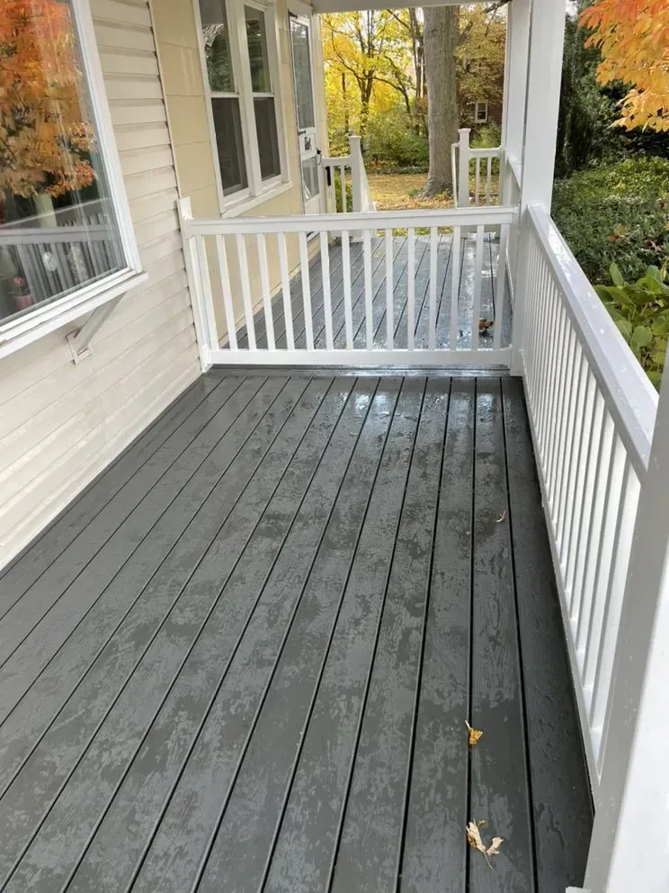 Gray wooden porch with white railing on a house, outdoor setting.