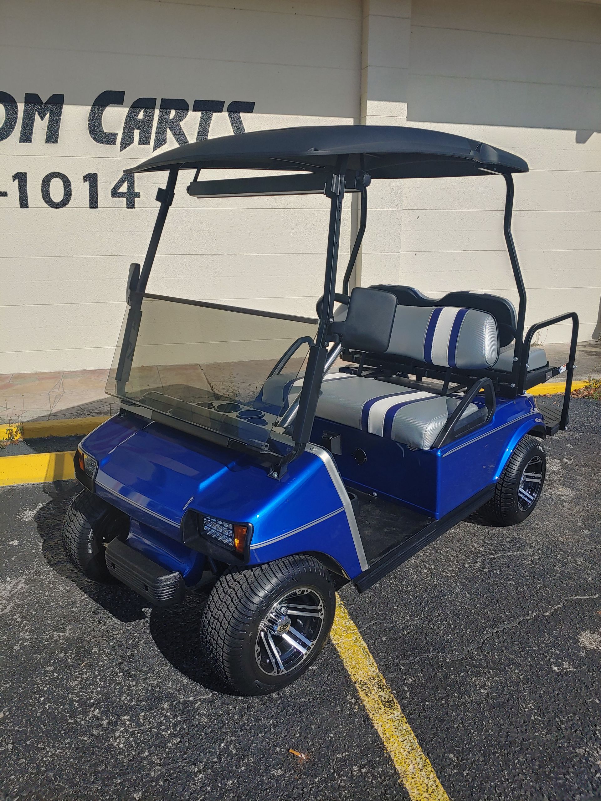 A royal blue golf cart with grey and white striped seats parked on a paved lot.
