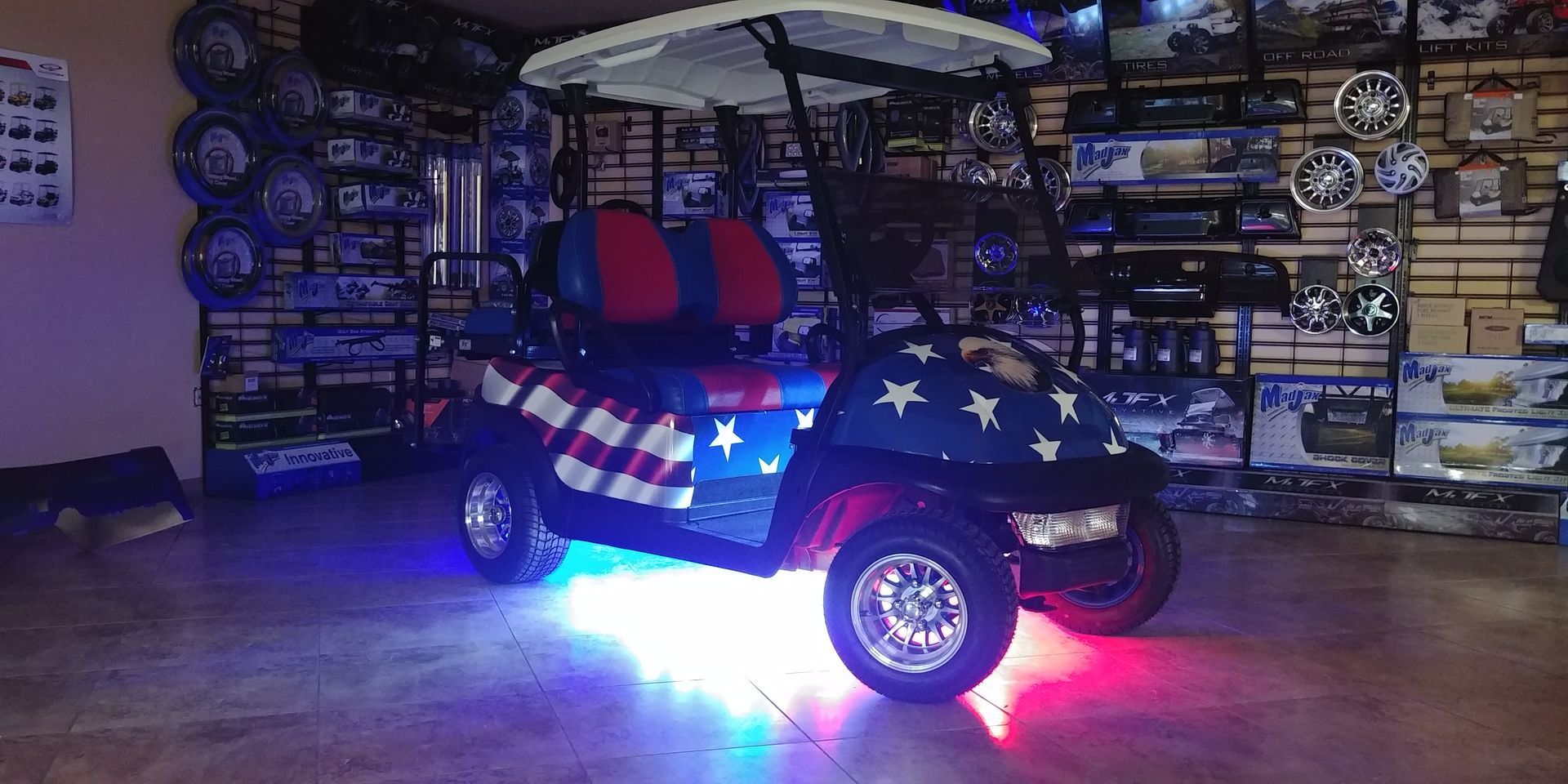 A golf cart with a red, white, and blue American flag theme and glowing underbody lights displayed in a shop.