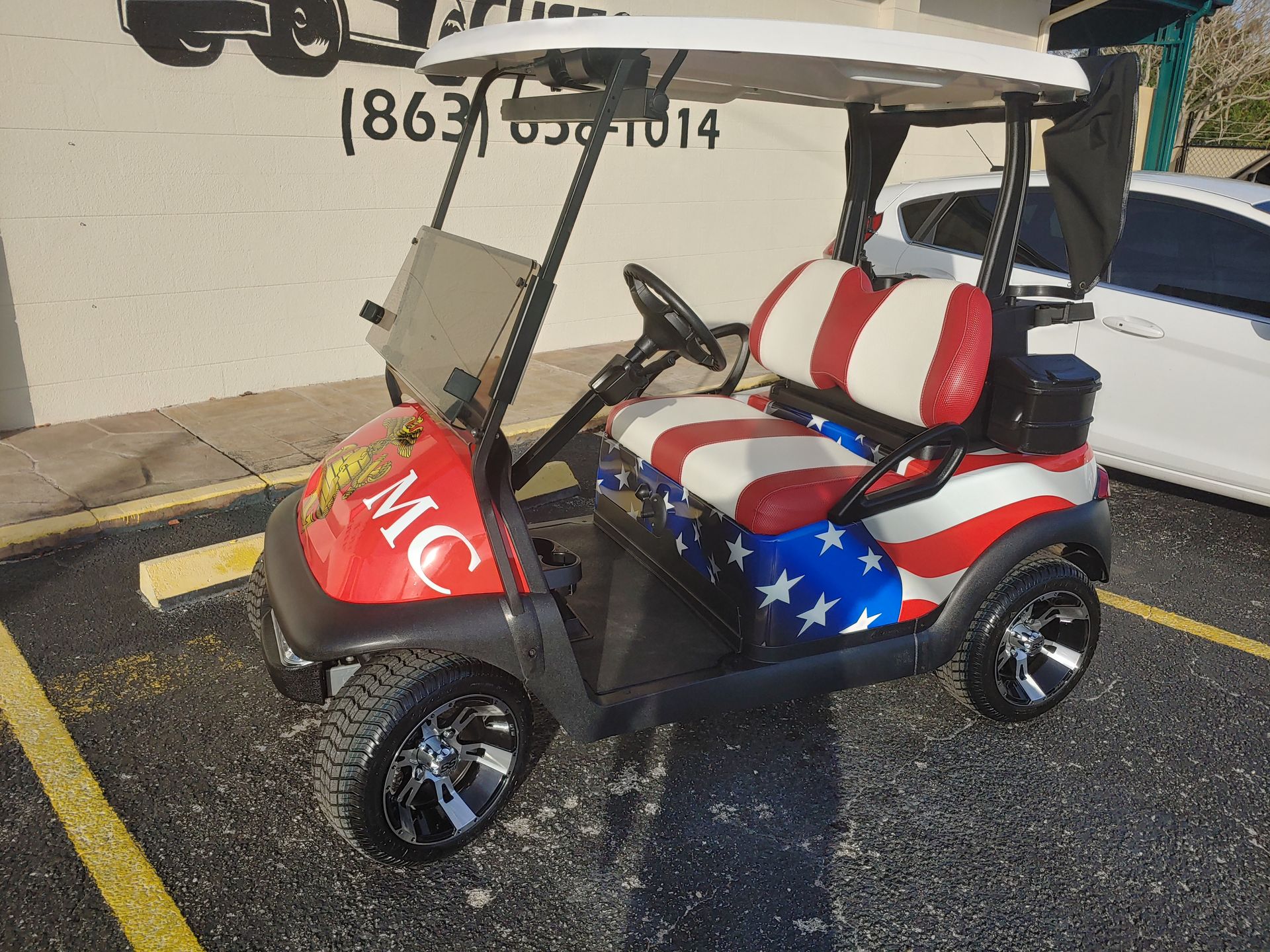 A golf cart customized with a red, white, and blue American flag theme and a Marine Corps emblem on its front hood.