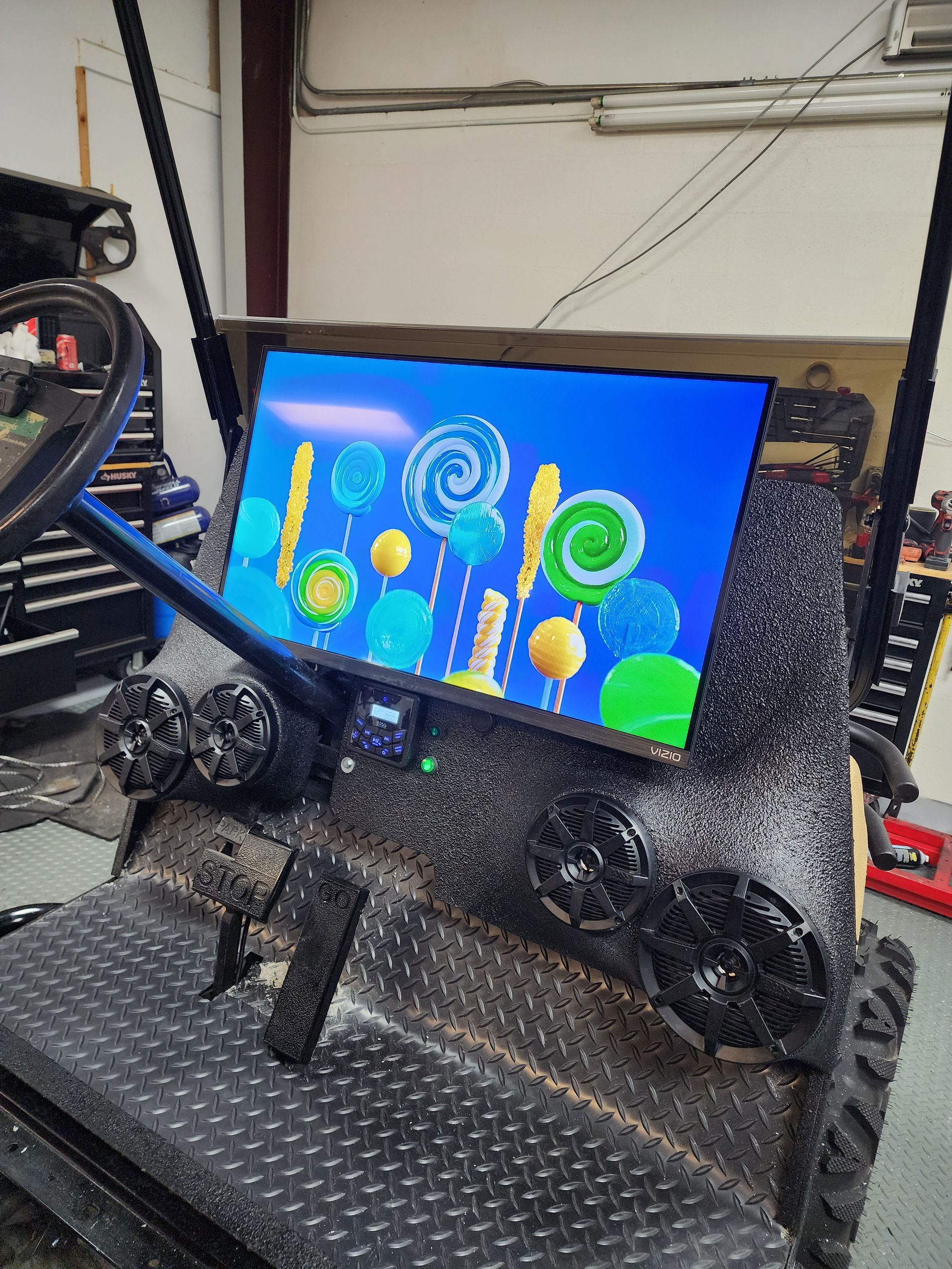 A television screen displaying colorful candy graphics is mounted on the textured dashboard of a modified golf cart.