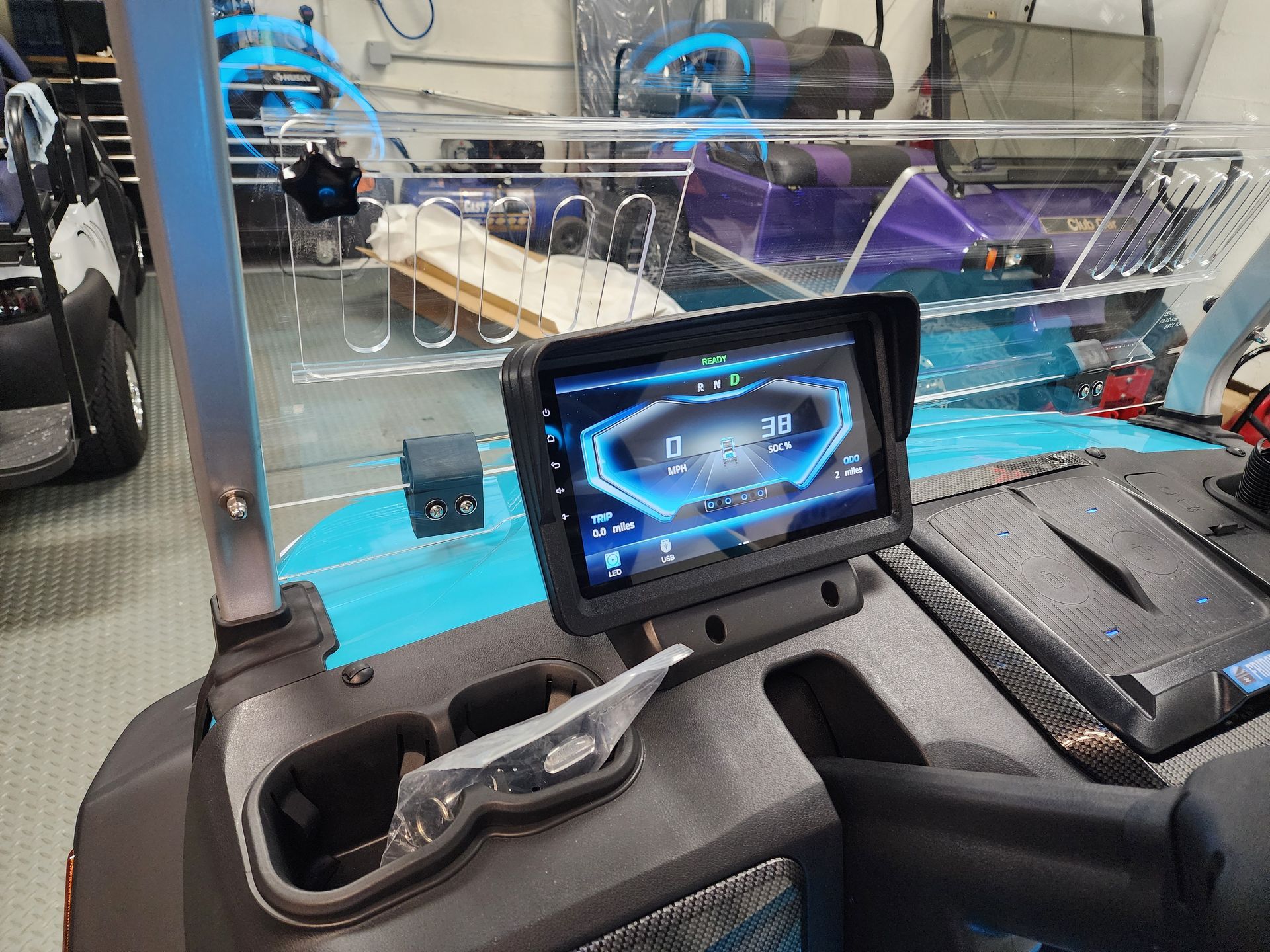 The digital dashboard display of a turquoise golf cart, featuring a bright blue interface inside a garage setting.