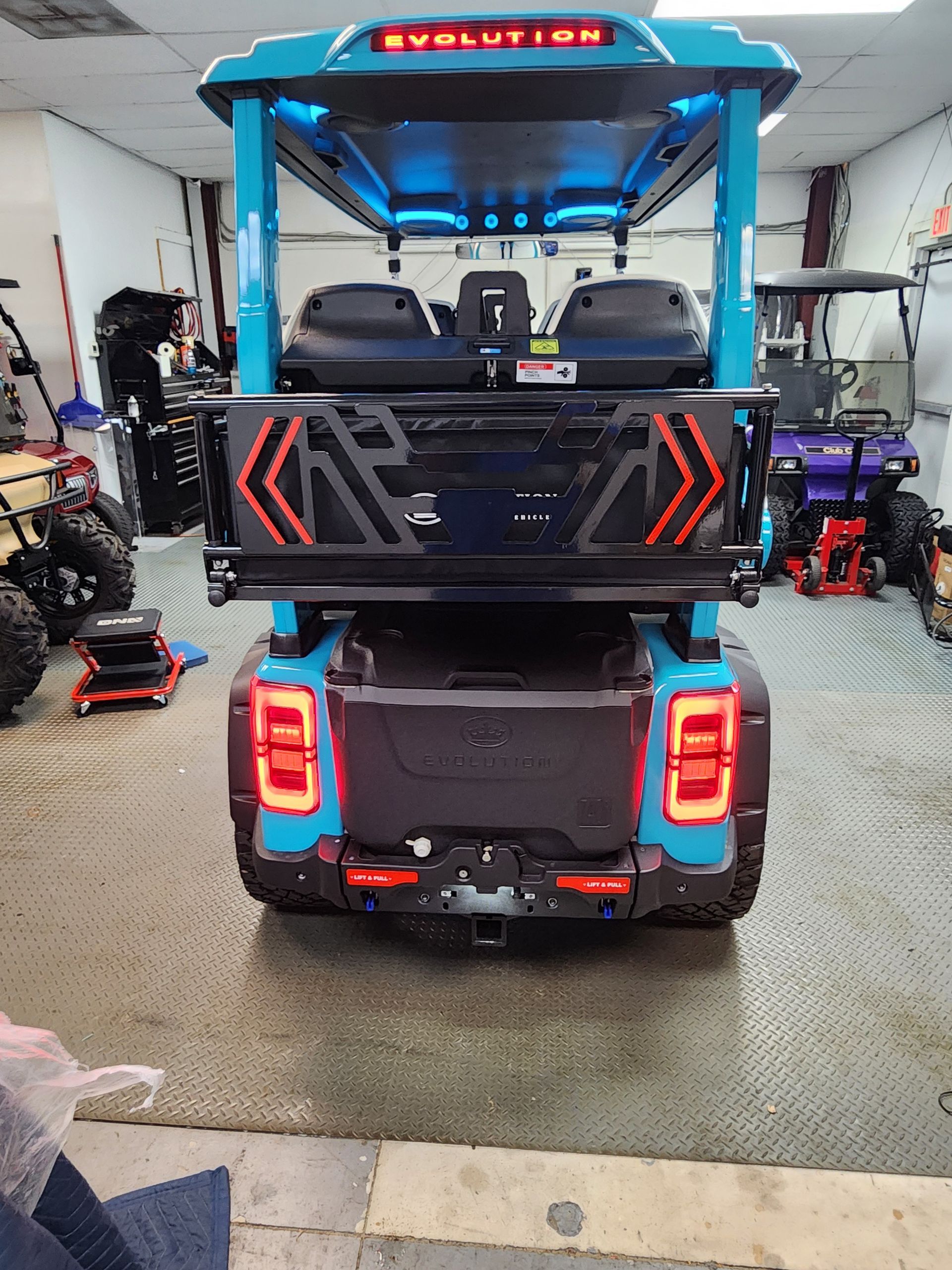 Rear view of a bright blue Evolution golf cart with LED tail lights, stored inside a shop.