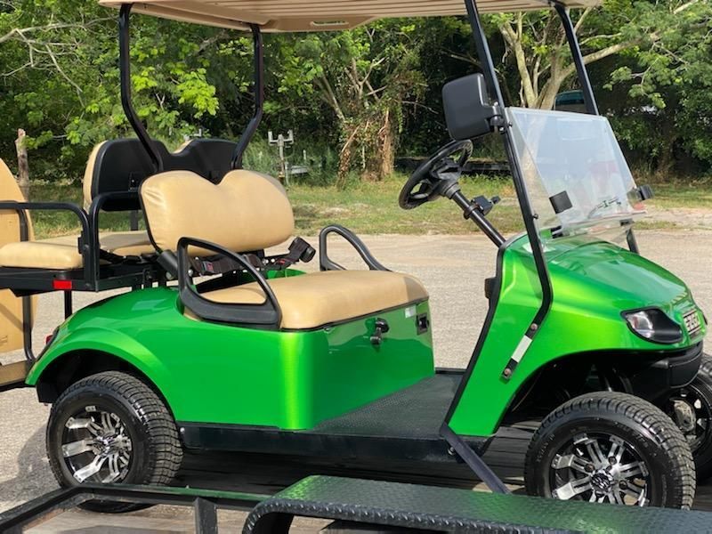 Green golf cart with tan seats, black accents, and chrome wheels parked outside.