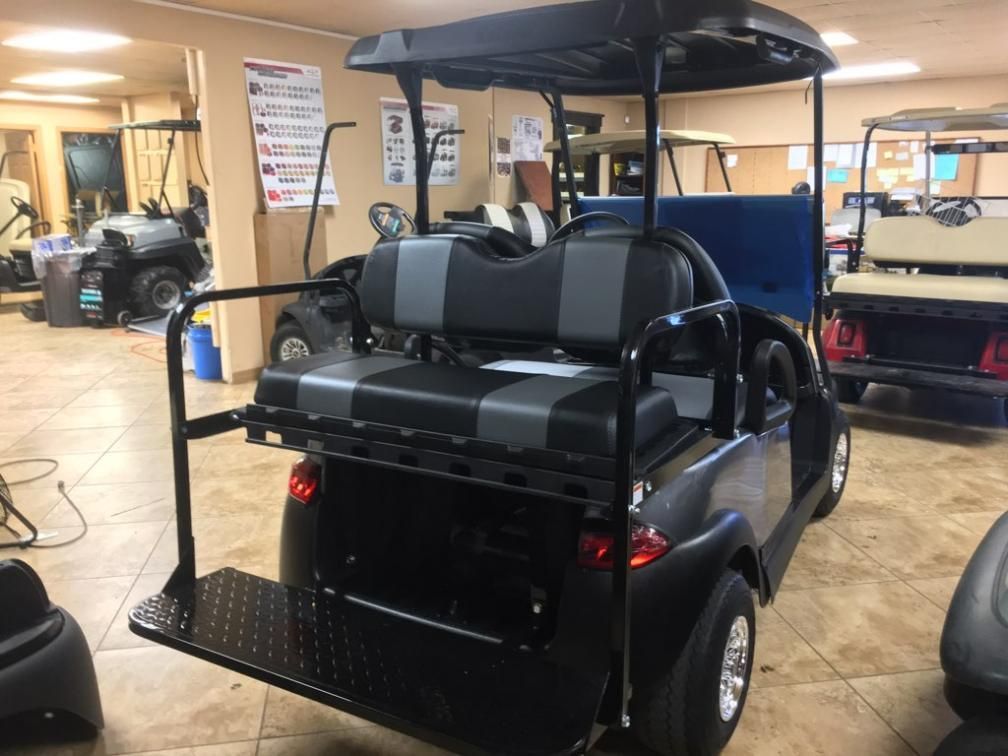 Black golf cart with gray and black seats, a cargo carrier, and a canopy inside a showroom.