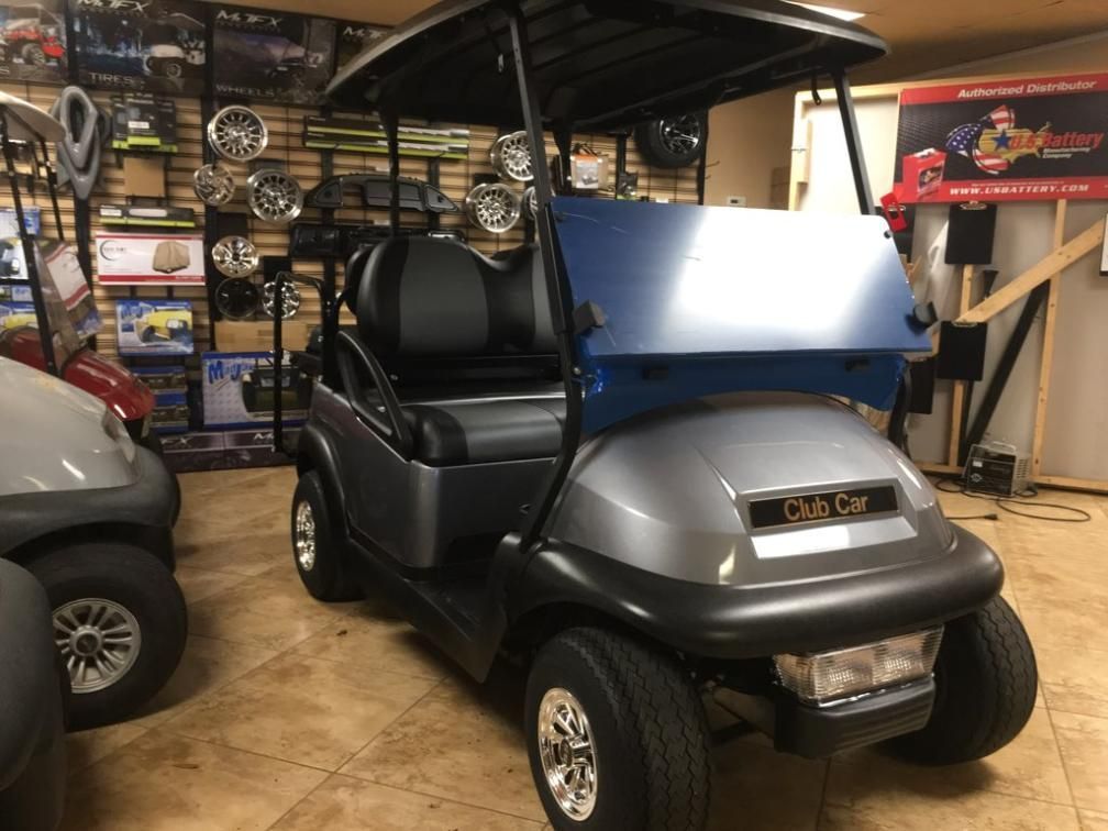 Gray and black Club Car golf cart with a blue windshield, indoors.