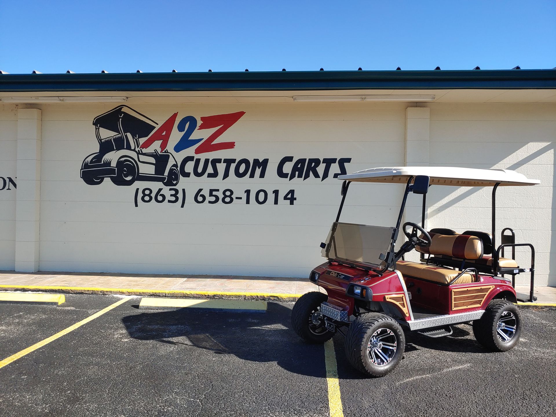 Red and tan golf cart parked outside A2Z Custom Carts storefront with logo and phone number.