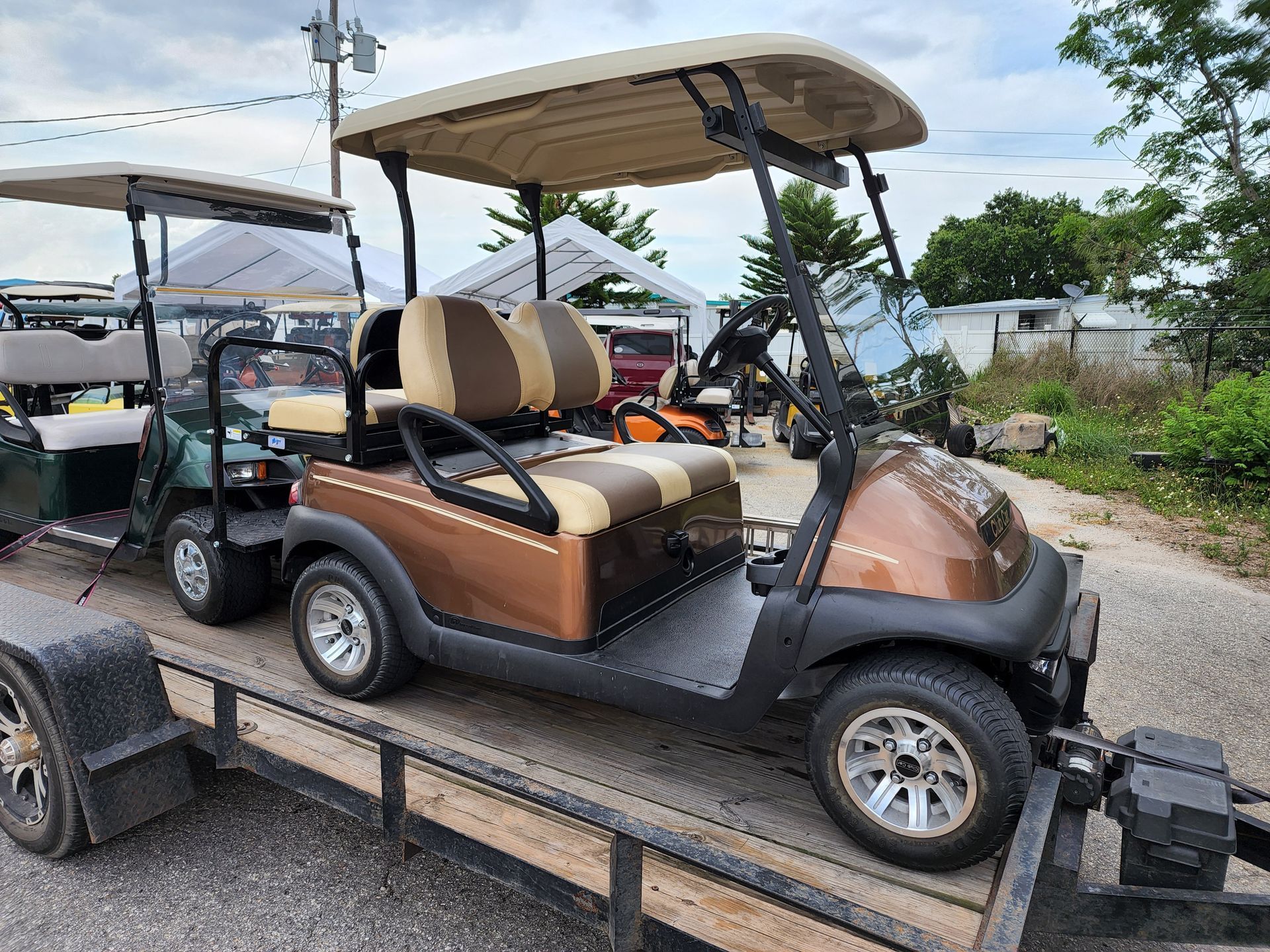 Two golf carts on a trailer. One is brown and tan, the other is green. Outdoor setting.