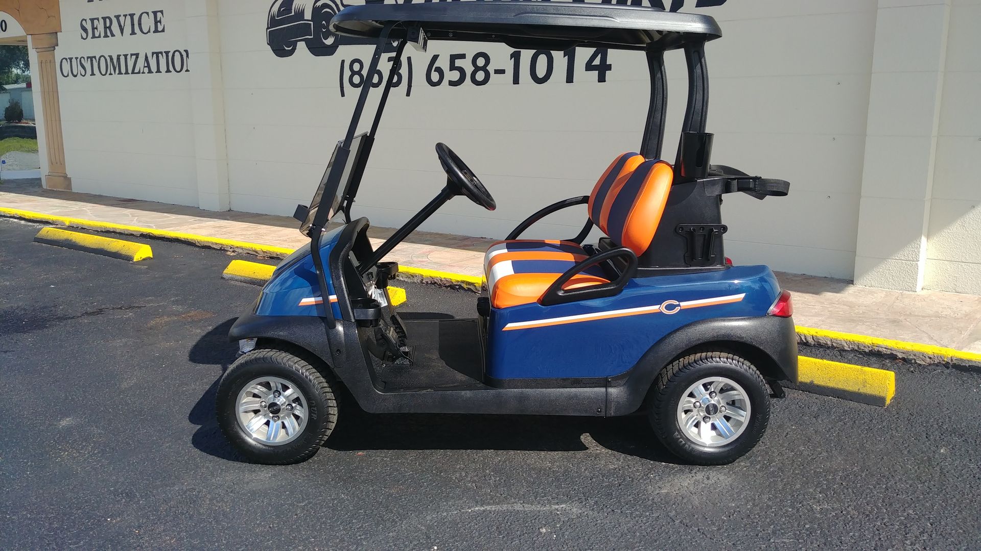 Blue and orange golf cart parked on asphalt, near a building.