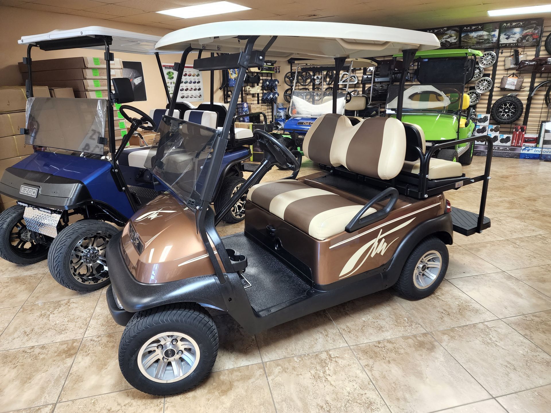 Golf carts of various colors inside a showroom. The main one is brown and beige.
