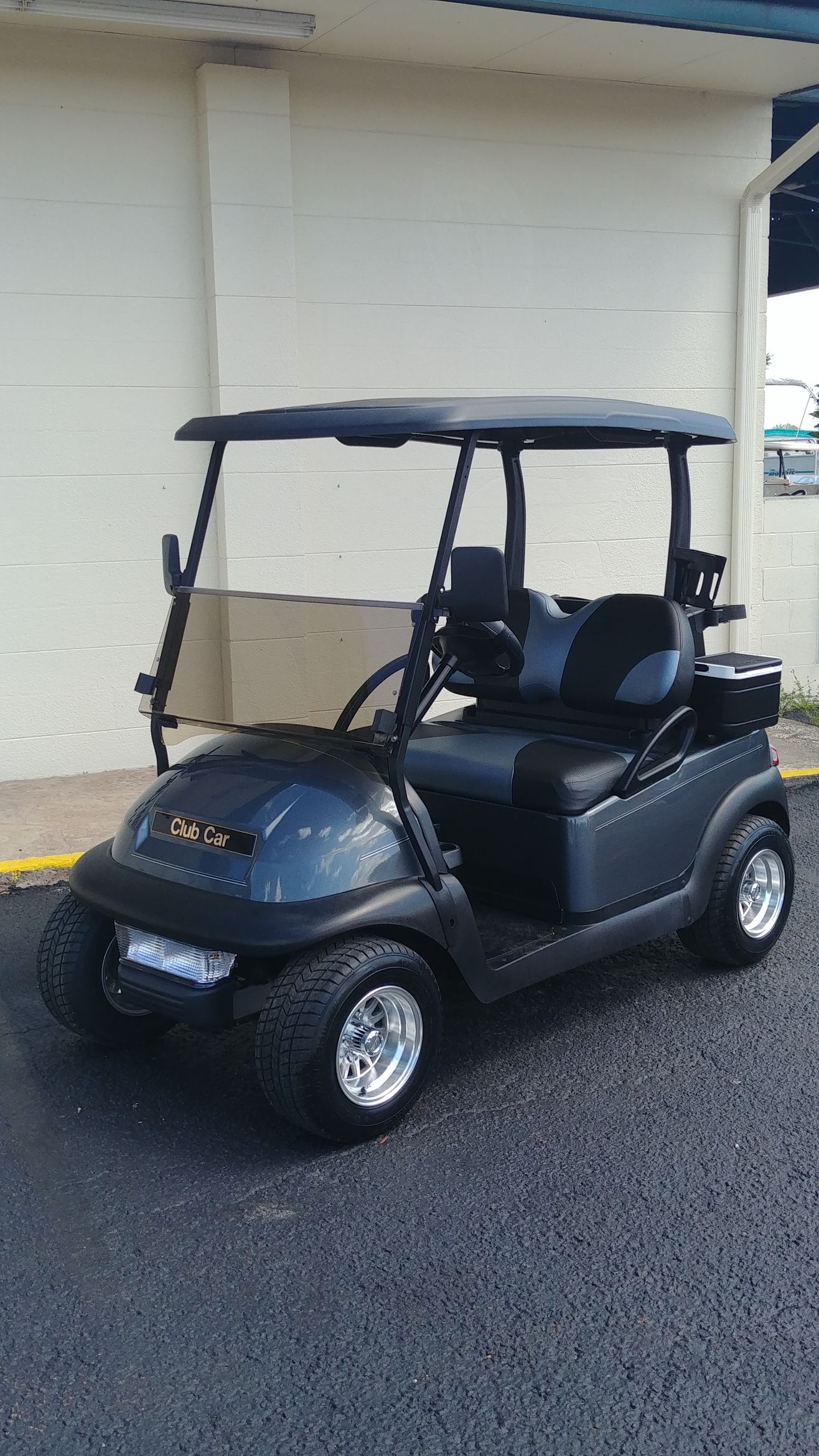 Black golf cart parked on asphalt, under a shaded area.