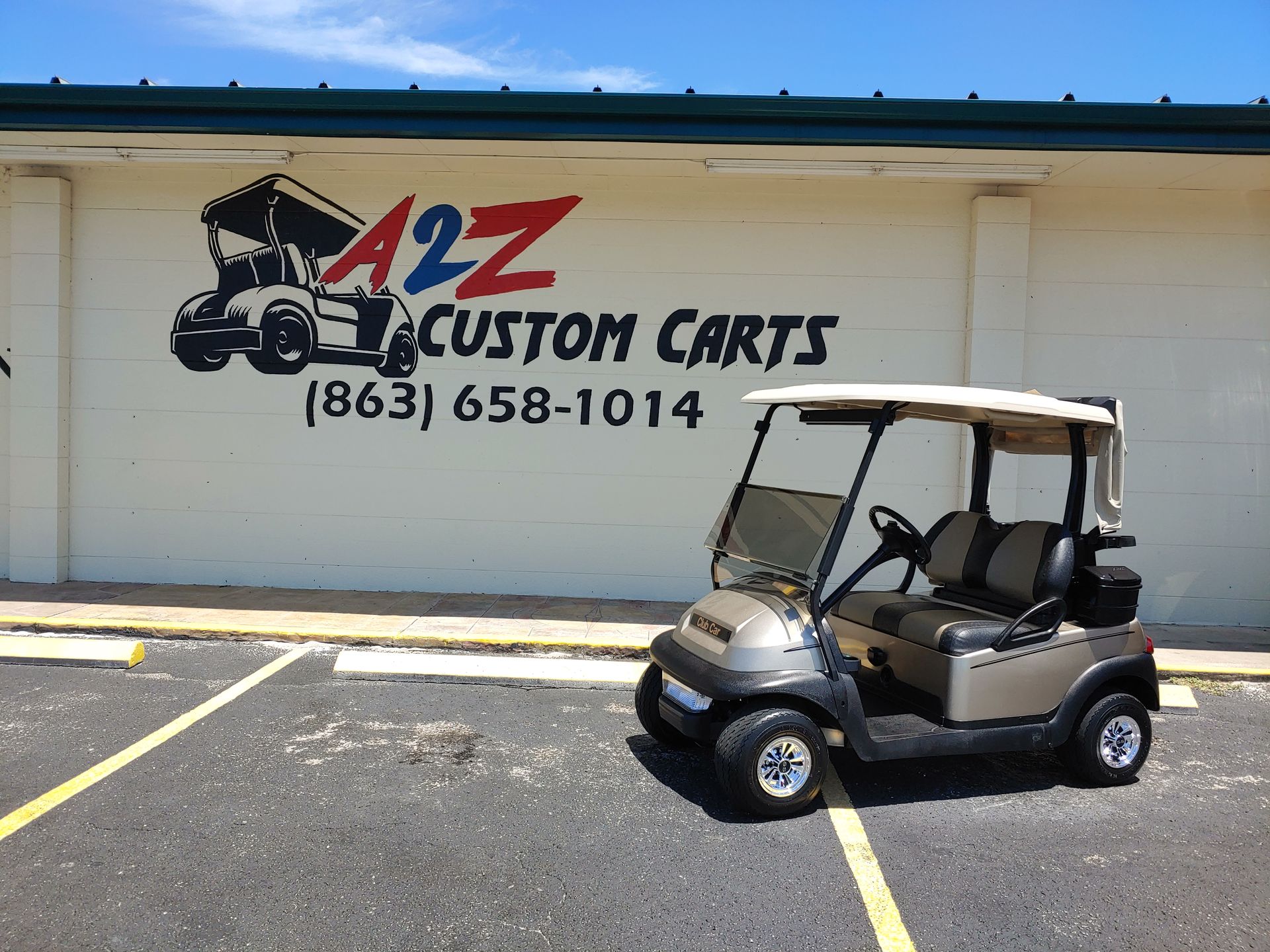 Golf cart parked in front of A2Z Custom Carts sign, tan and black cart.