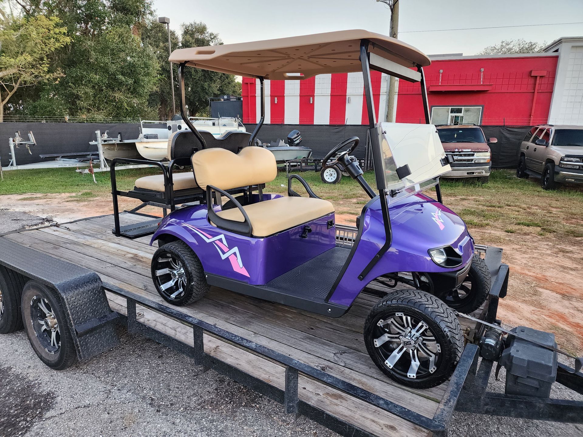 Purple golf cart with tan seats and roof on a trailer.