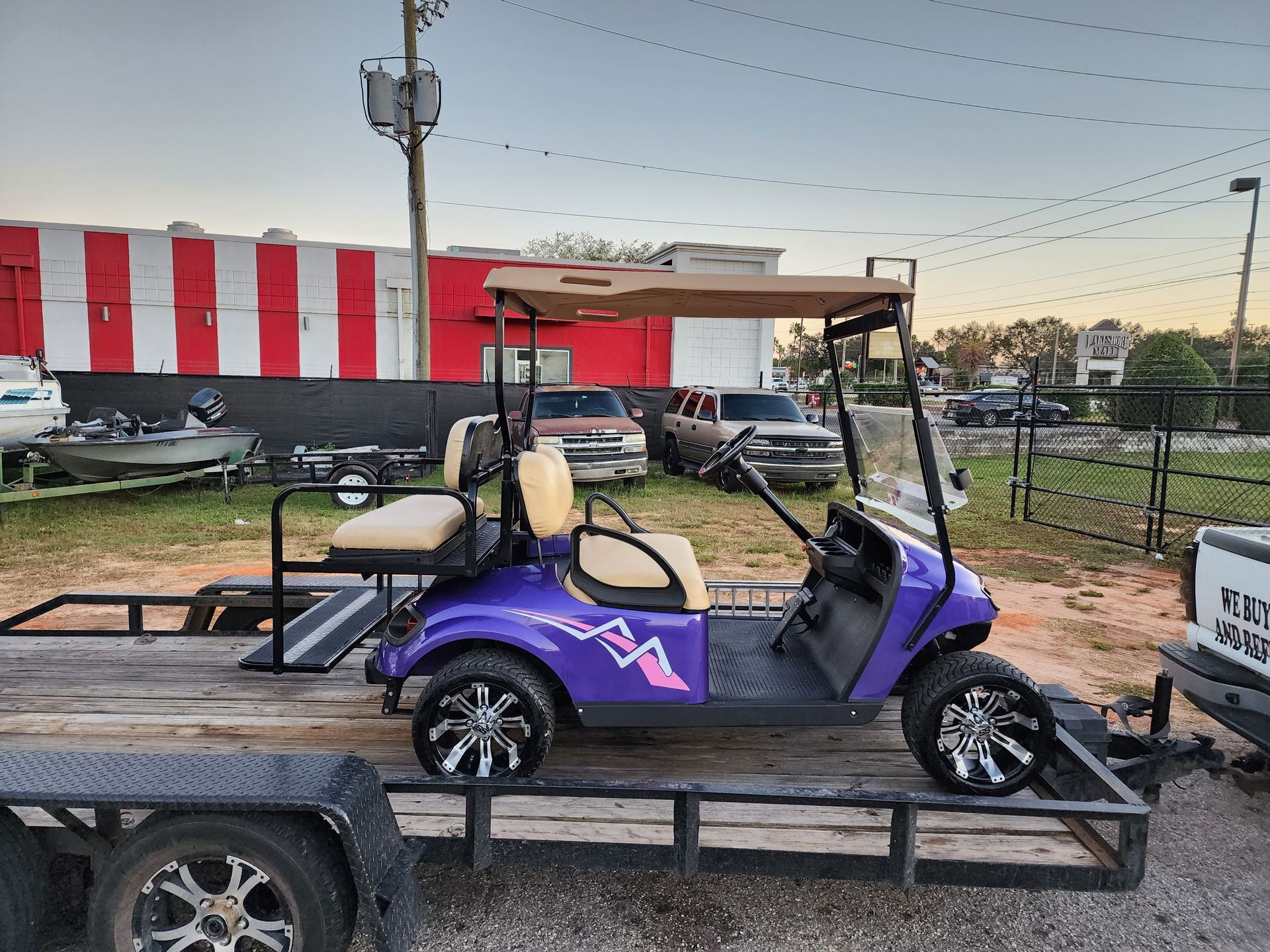 Purple golf cart with custom wheels on a trailer, beige seats, a tan canopy, outside.