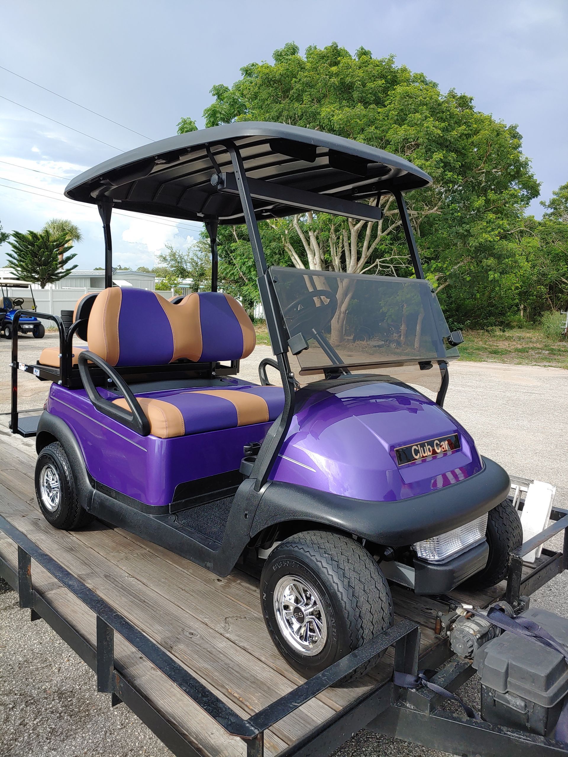 Purple golf cart on a trailer, with a black roof, and brown and purple seats.