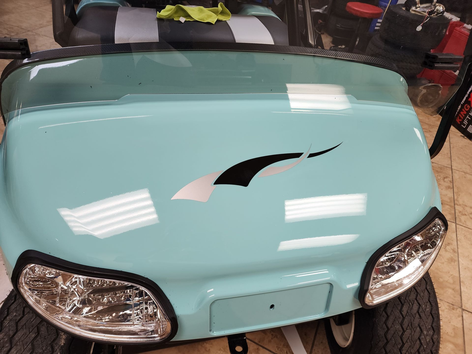 Light blue golf cart with a black and silver decal on the hood.