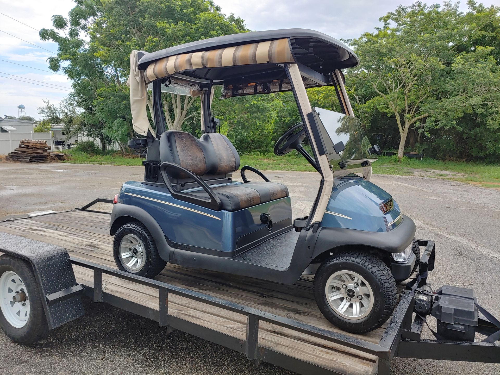 Blue golf cart with tan roof, on a trailer.