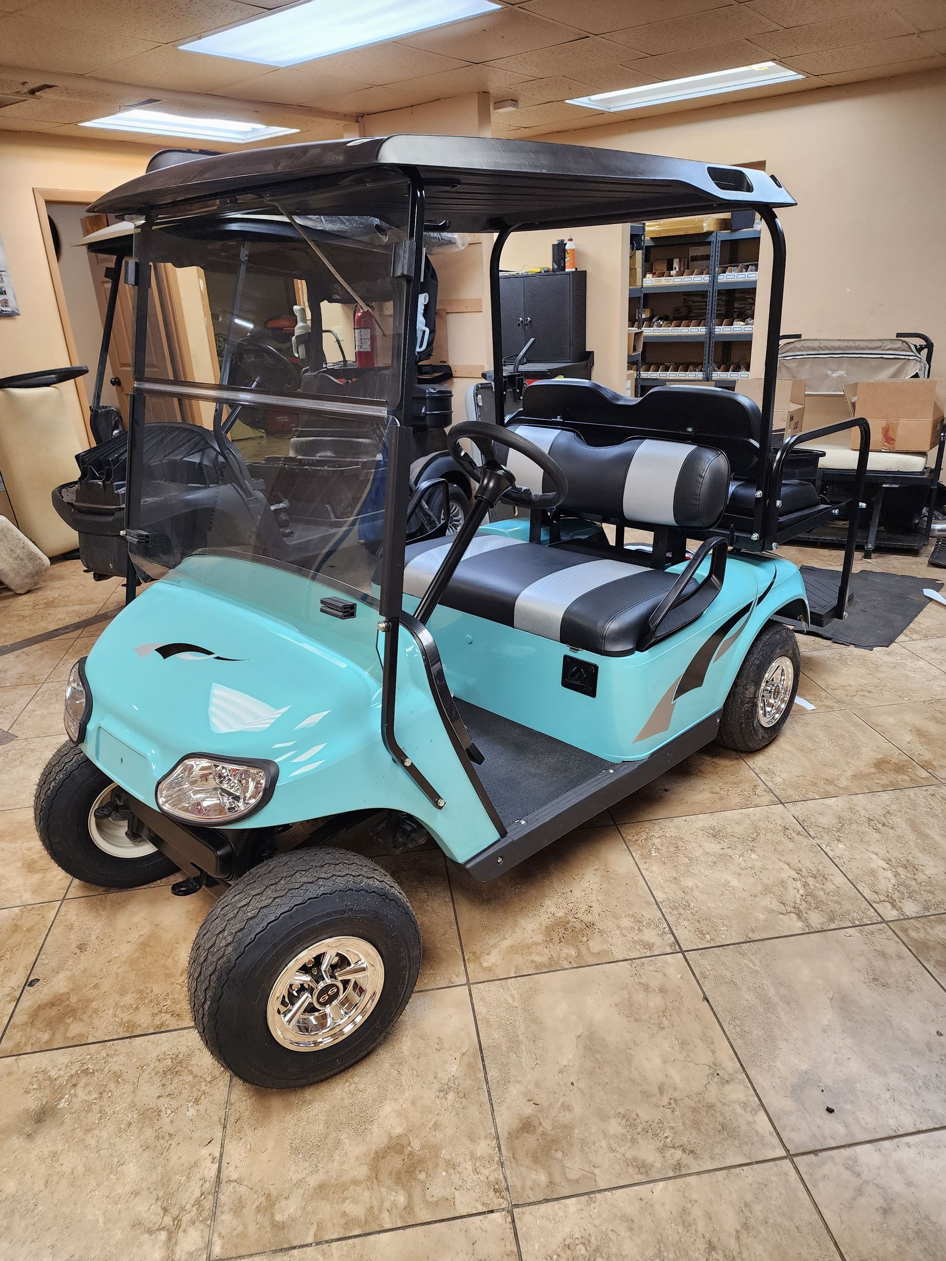 A light blue golf cart with black accents, black roof, and off-road tires, parked indoors.