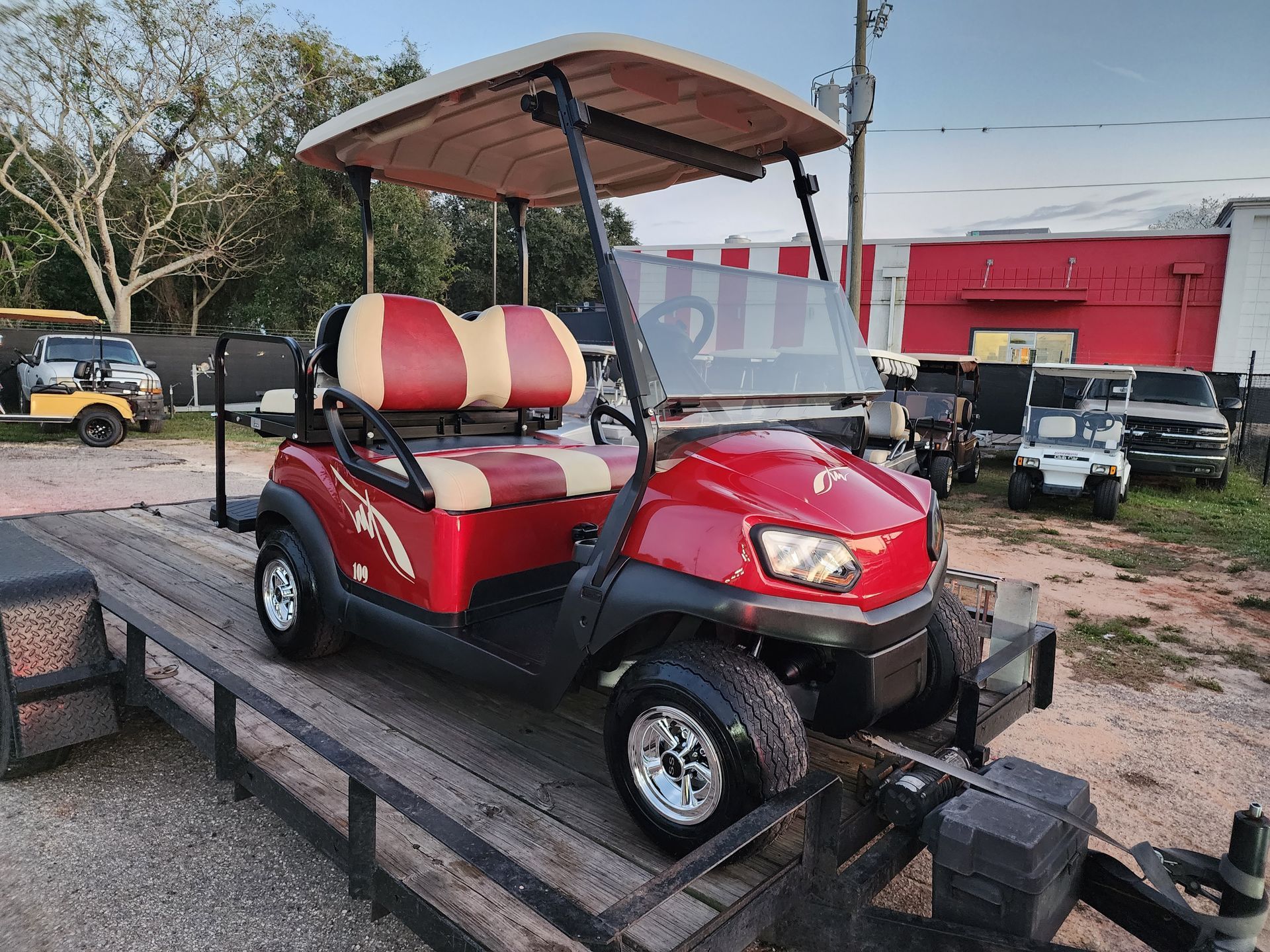 Red golf cart on a trailer, with a tan roof and red and beige seats.