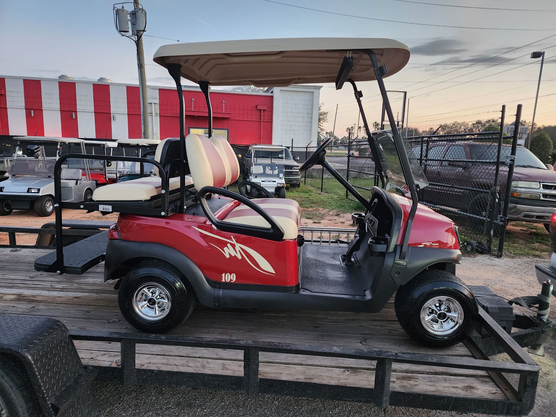 Red golf cart with tan roof, on a trailer.